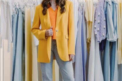 Ragazza indossa un outfit con blazer oversize giallo, top arancione e jeans chiari davanti a un appendiabiti, per la guida su come indossare i capi del guardaroba femminile.