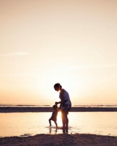 Una mamma insegna a camminare al suo bambino in riva al mare al tramonto.