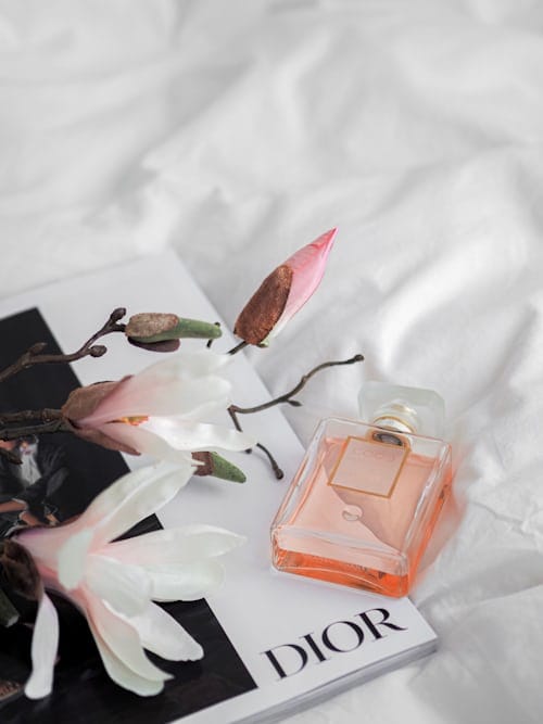 Flacone di profumo da donna su tessuto bianco, fiori e rivista con testo Dior