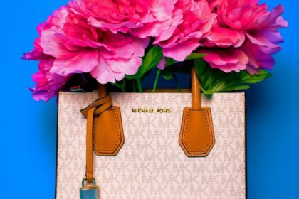 Borsa a mano Michael Kors con motivo logato bianco e dettagli in pelle marrone, riempita con grandi fiori fucsia su sfondo azzurro.