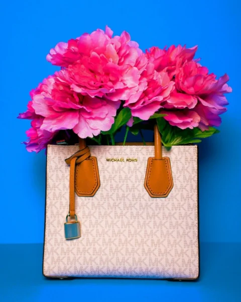 Borsa a mano Michael Kors con motivo logato bianco e dettagli in pelle marrone, riempita con grandi fiori fucsia su sfondo azzurro.