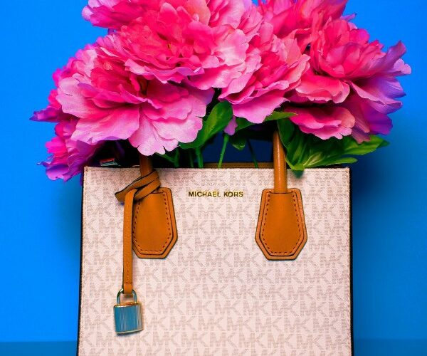 Borsa a mano Michael Kors con motivo logato bianco e dettagli in pelle marrone, riempita con grandi fiori fucsia su sfondo azzurro.