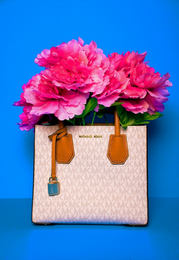 Borsa a mano Michael Kors con motivo logato bianco e dettagli in pelle marrone, riempita con grandi fiori fucsia su sfondo azzurro.