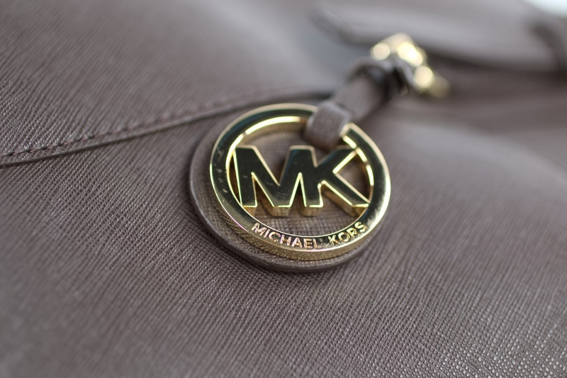Dettaglio ciondolo logo Michael Kors su borsa donna in pelle taupe