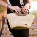 Esempio di borse estive Amazon: dettaglio di una borsa estiva in paglia intrecciata con manici in legno e tracolla ricamata, abbinata a un tubino nero.