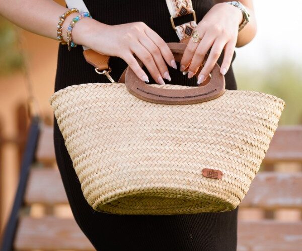 Esempio di borse estive Amazon: dettaglio di una borsa estiva in paglia intrecciata con manici in legno e tracolla ricamata, abbinata a un tubino nero.