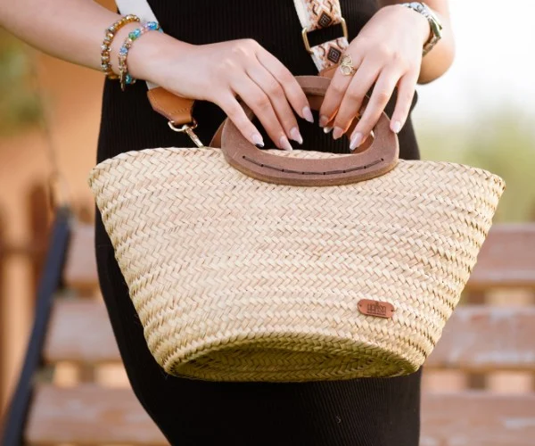 Esempio di borse estive Amazon: dettaglio di una borsa estiva in paglia intrecciata con manici in legno e tracolla ricamata, abbinata a un tubino nero.