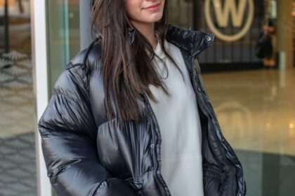 Ragazza indossa un giubbino oversize tra i 5 modelli di giubbini invernali di tendenza in colore grigio scuro, jeans e felpa oversize bianca