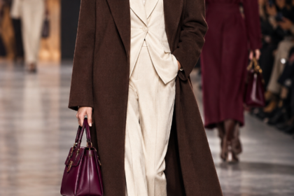 Modella in passerella con i colori moda Autunno Inverno 2026-2027: cappotto marrone cioccolato, tailleur crema e borsa berry