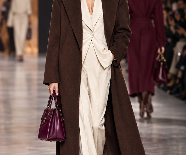 Modella in passerella con i colori moda Autunno Inverno 2026-2027: cappotto marrone cioccolato, tailleur crema e borsa berry