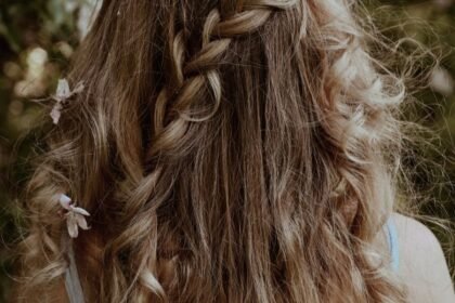 Chioma folta con capelli lunghi e sani intrecciati decorati con fiori rosa per la guida agli integratori per capelli