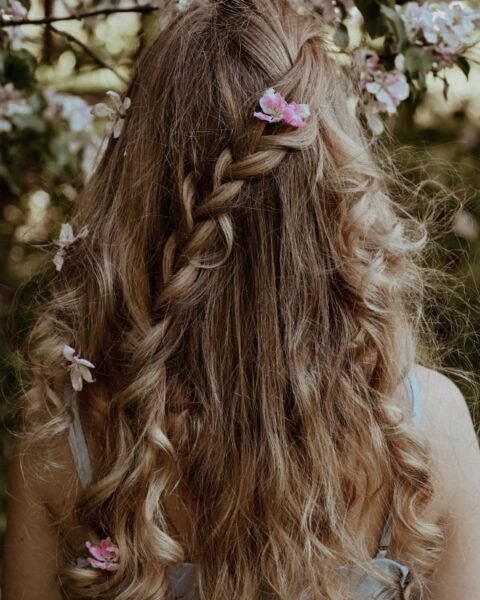 Chioma folta con capelli lunghi e sani intrecciati decorati con fiori rosa per la guida agli integratori per capelli