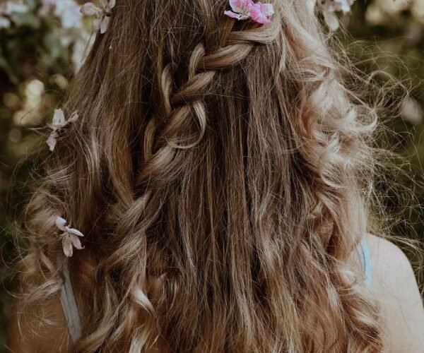 Chioma folta con capelli lunghi e sani intrecciati decorati con fiori rosa per la guida agli integratori per capelli
