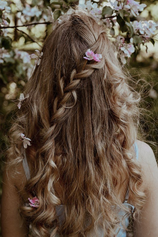 Chioma folta con capelli lunghi e sani intrecciati decorati con fiori rosa per la guida agli integratori per capelli