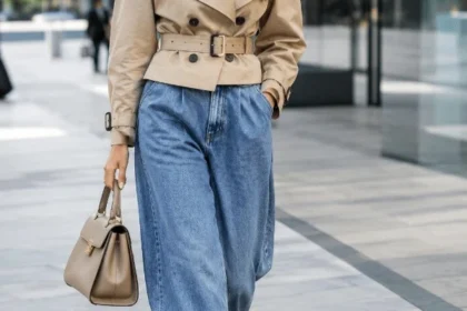 Donna con jeans balloon, trench corto stretto in vita e décolleté con tacco in un outfit metropolitano.